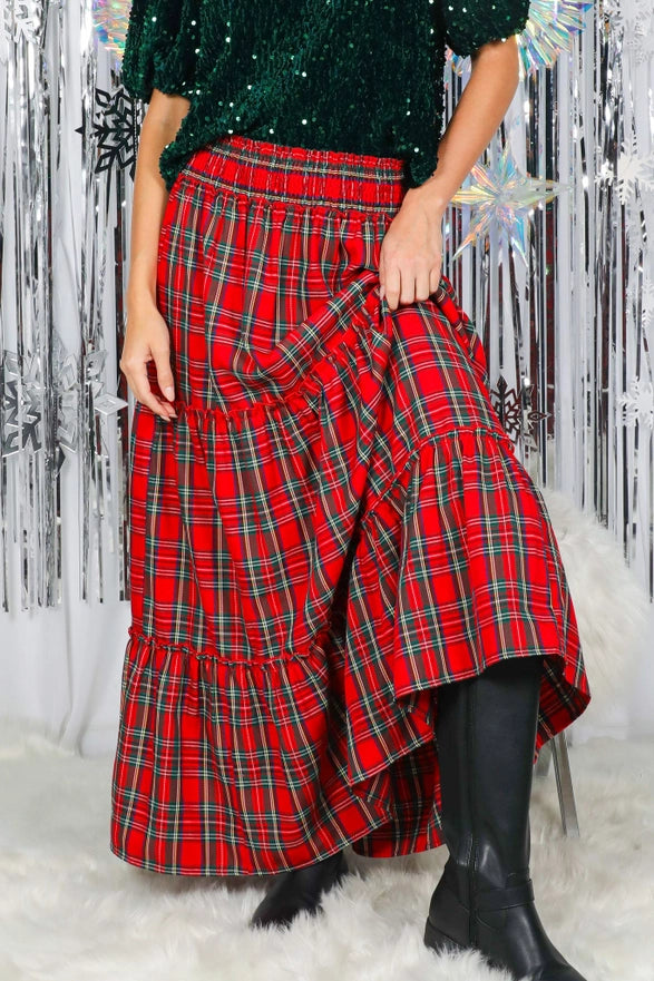 Person wearing a red plaid skirt with a green sequined top against a decorative silver and white background.