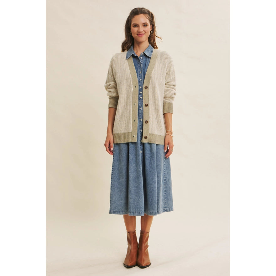 Woman wearing a beige cardigan over a denim dress on a plain background