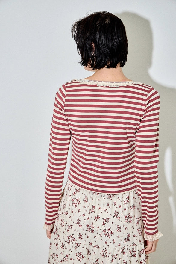 Person wearing a red and white striped long-sleeve top with a floral skirt against a plain background