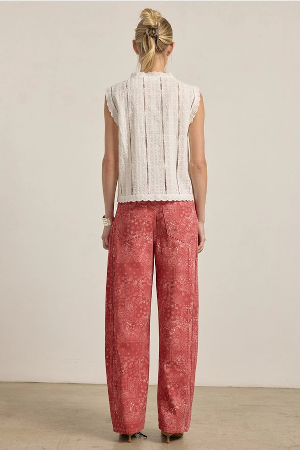 Person wearing a white sleeveless top and red patterned pants against a plain background