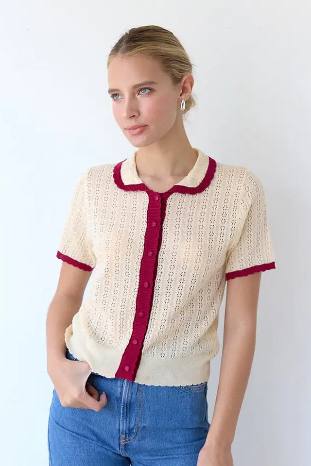 Woman wearing a cream lace cardigan with red trim against a white background