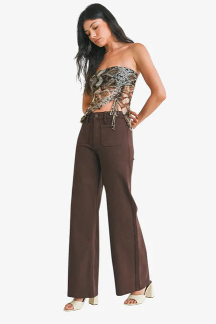 Woman wearing a strapless top with snake print and brown wide-leg pants on a white background