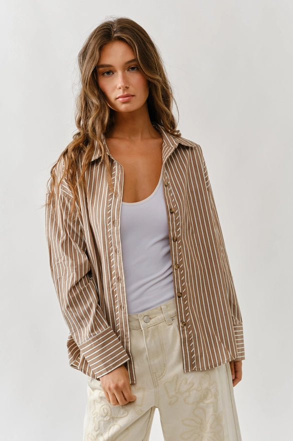 Woman wearing a striped shirt over a tank top with light pants on a plain background