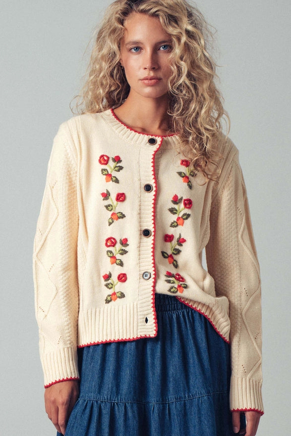 Woman wearing a cream cardigan with floral embroidery on a gray background