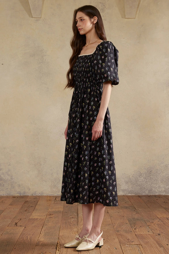 Woman wearing a black floral dress standing against a beige wall.