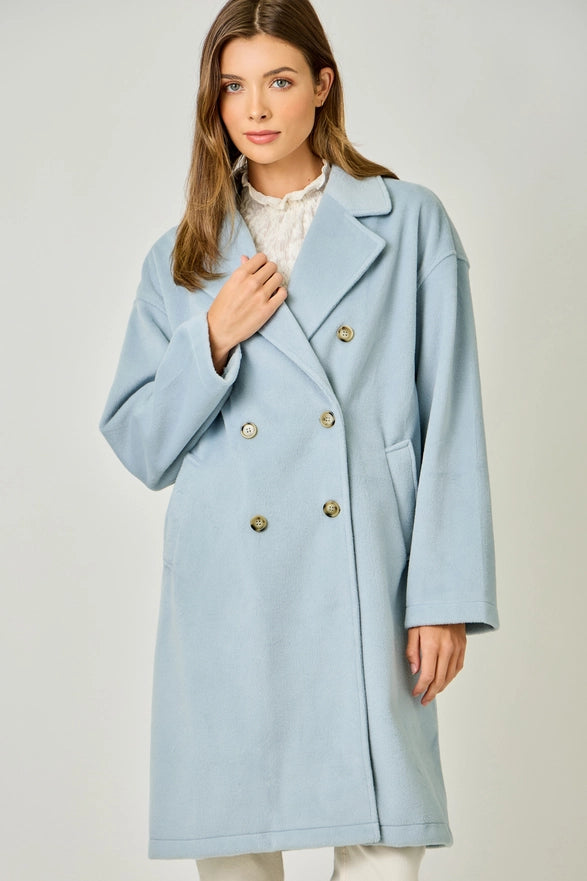 Woman wearing a light blue coat with gold buttons on a plain background