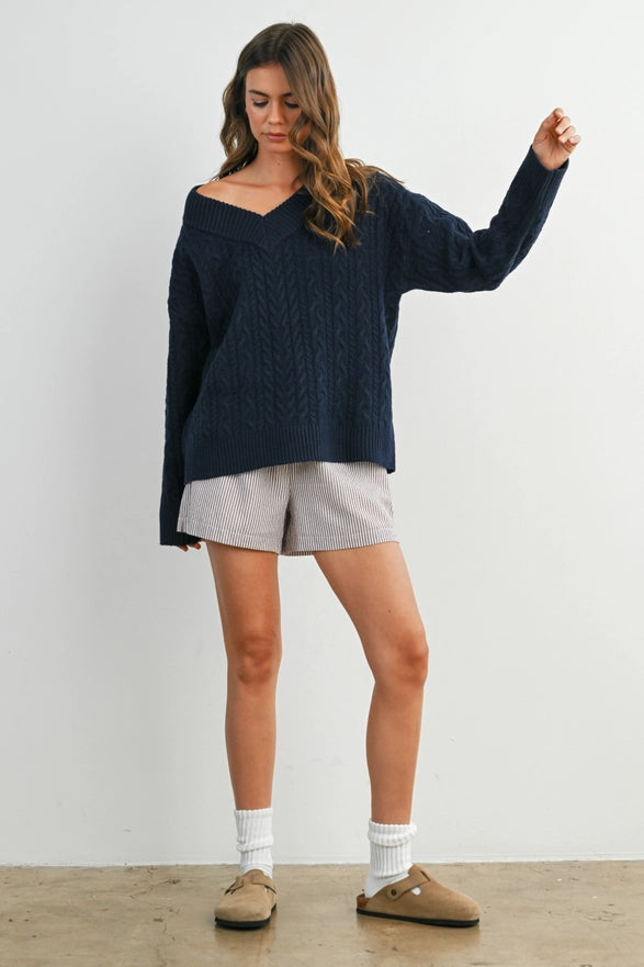 Girl Standing against a plain background wearing a V neck Navy Blue cable knit sweater with long sleeve