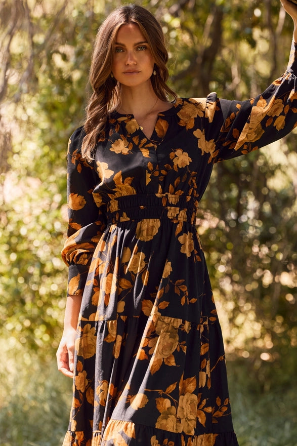 Woman wearing a dark floral dress standing outdoors with trees in the background
