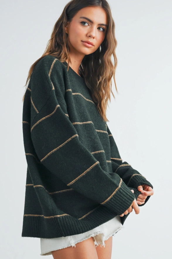 Woman wearing a dark green sweater with light brown stripes on a plain background