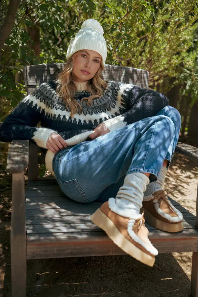 Person wearing a patterned sweater, jeans, and UGG boots sitting outdoors.