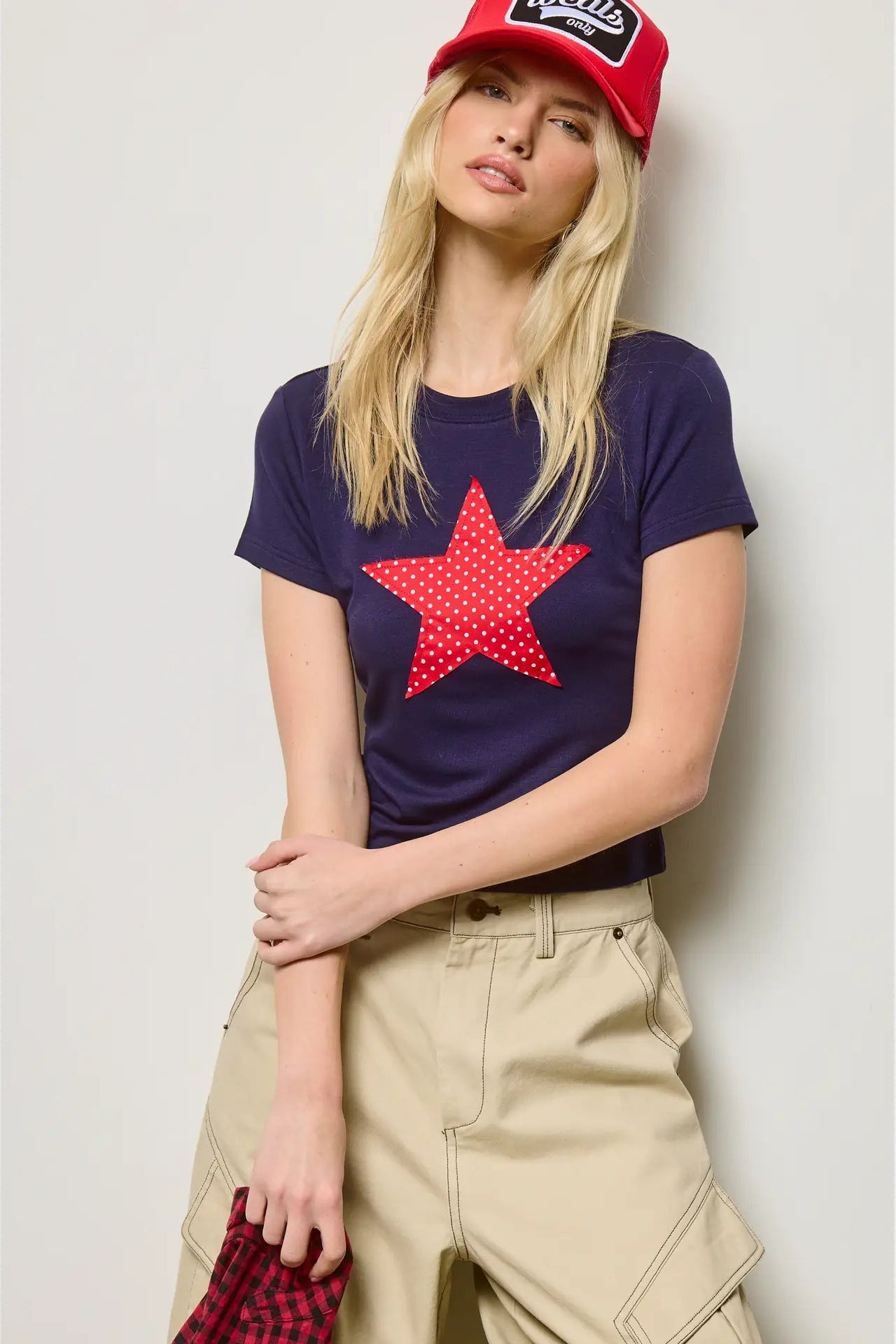 Woman wearing a navy t-shirt with a red star, beige pants, and a red cap against a light background