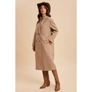 Woman wearing a beige coat and brown hat against a beige background