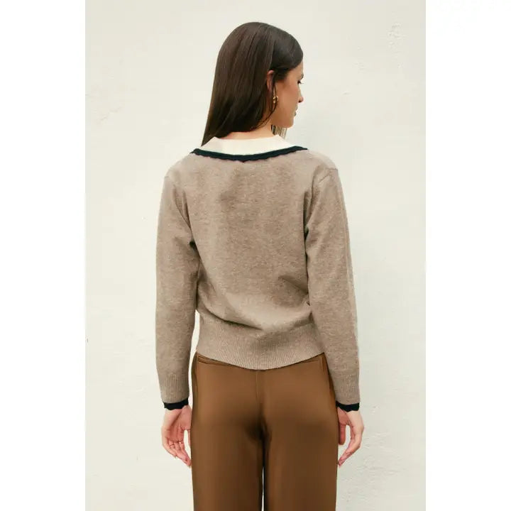 Woman wearing a beige sweater with black trim and brown pants on a plain background