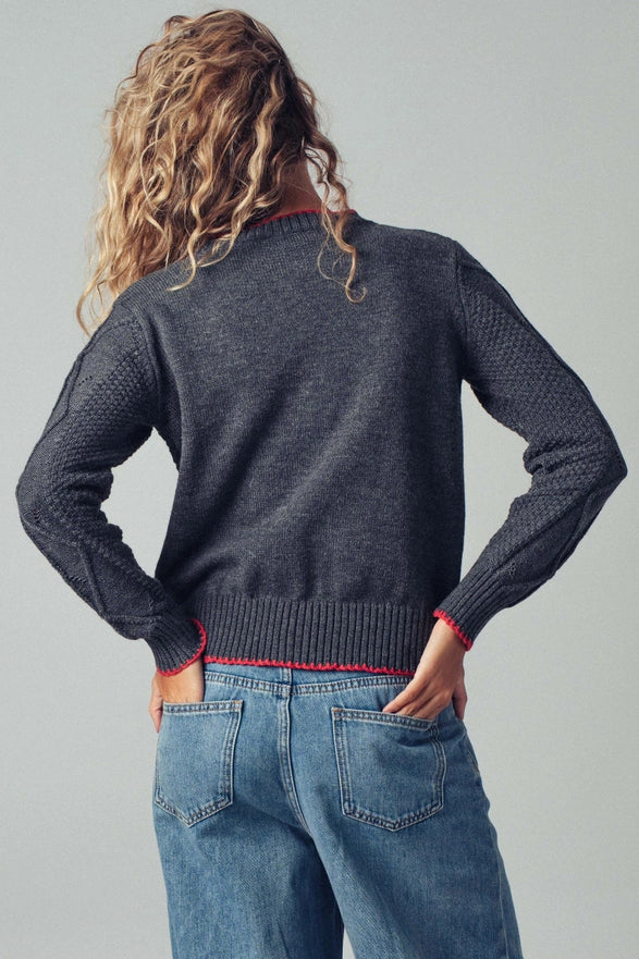 Person wearing a dark gray sweater and blue jeans against a plain background