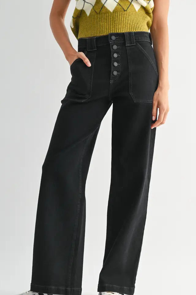 Black wide-leg jeans with button details worn by a person on a light gray background