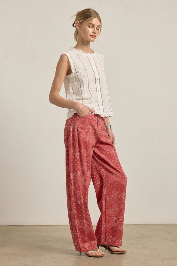 Woman wearing a white sleeveless top and red patterned pants against a plain background