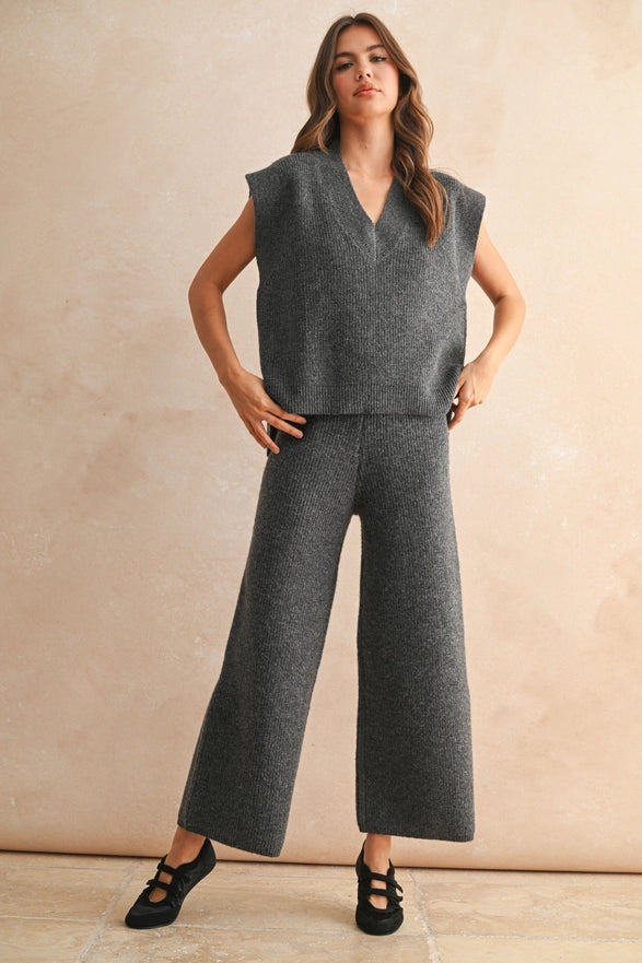 Woman wearing a gray sleeveless top and wide-leg pants against a beige background