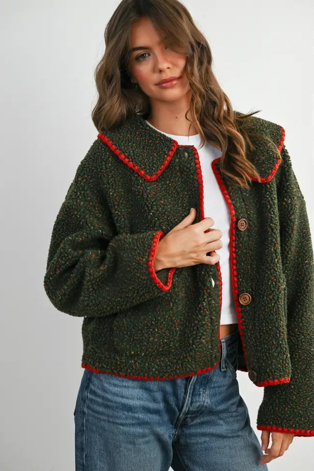 Woman wearing a green knitted cardigan with red trim on a white background