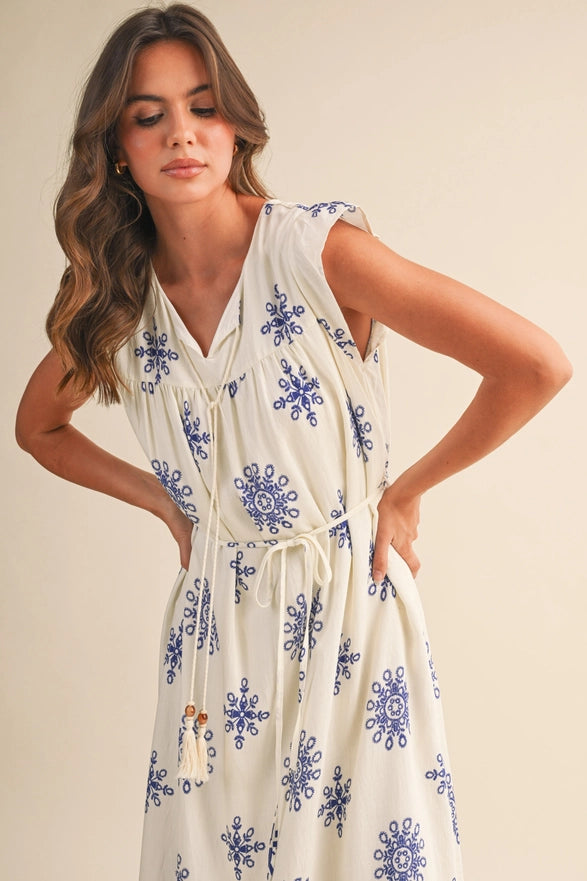 Woman wearing a white dress with blue floral patterns against a beige background