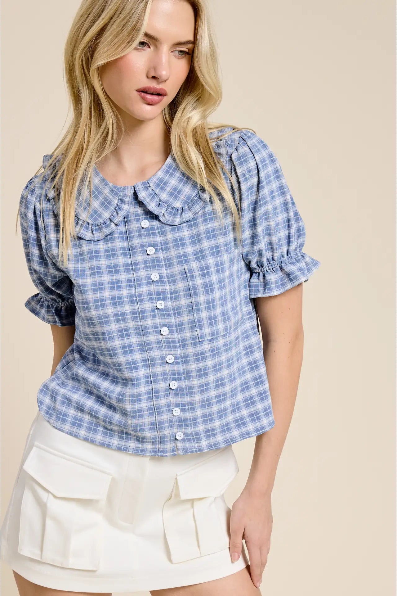 Woman wearing a blue plaid shirt with ruffled sleeves on a beige background