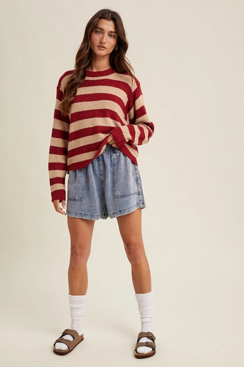 Woman wearing a red and beige striped sweater with denim shorts on a plain background