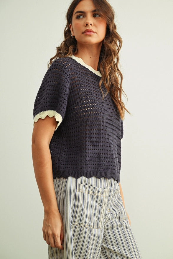 Woman wearing a navy blue crochet top with white trim on a light background