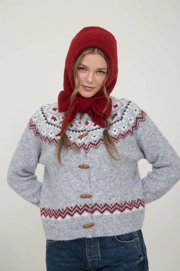 Person wearing a gray sweater with red patterns and a matching red hat and scarf on a white background