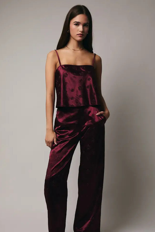 Woman wearing a burgundy satin top and pants against a plain background