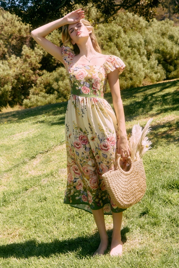 Woman in a floral dress standing in a grassy field with trees in the background