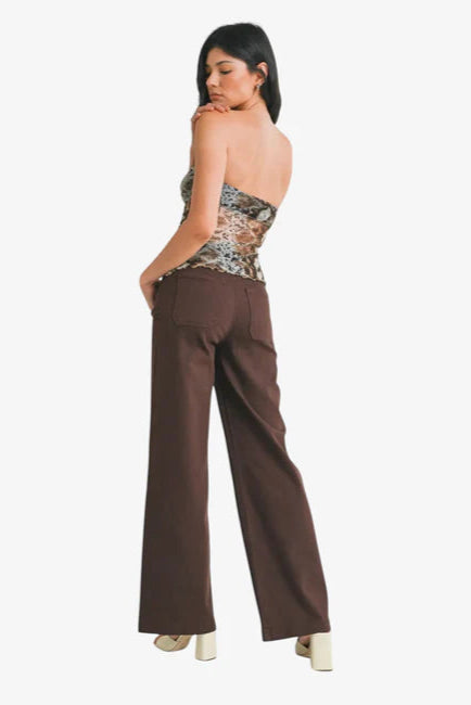 Woman wearing a patterned top and brown pants on a white background