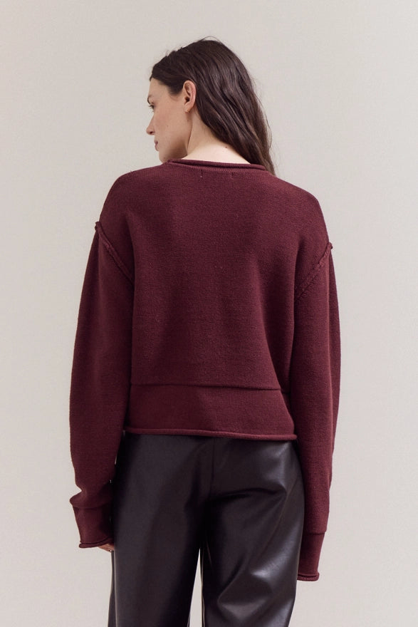 Person wearing a burgundy sweater and black pants on a plain background