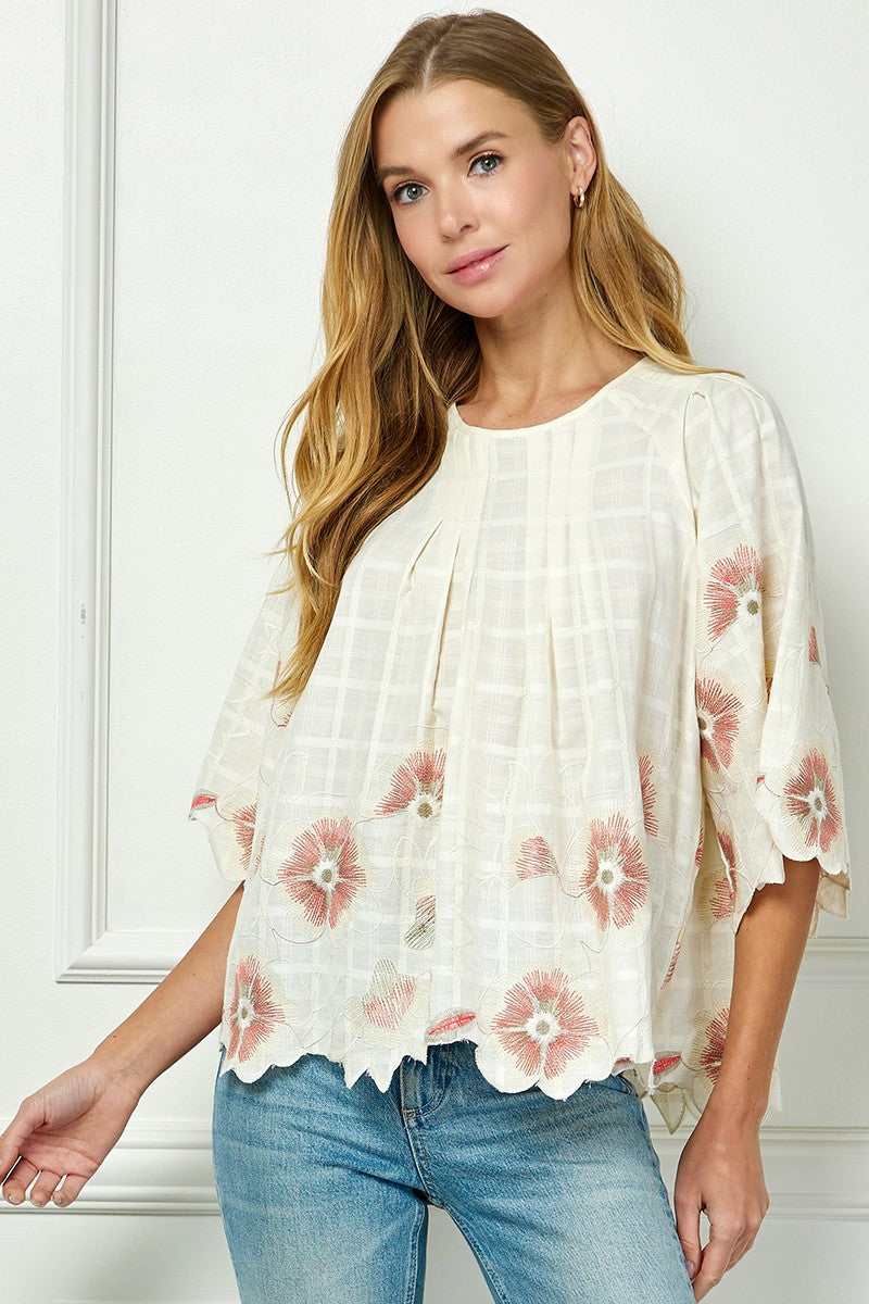 Woman wearing a white blouse with floral patterns and blue jeans against a white background