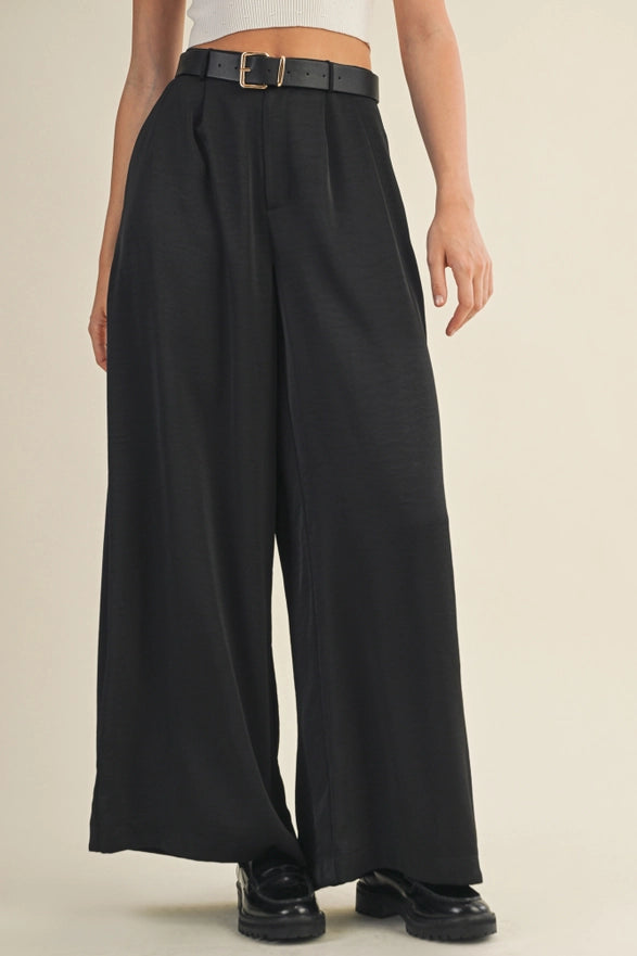 Person wearing black wide-leg pants with a beige background