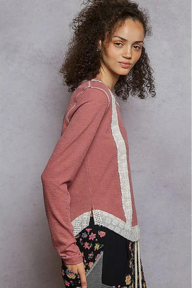 Woman wearing a pink sweater with lace details against a gray background