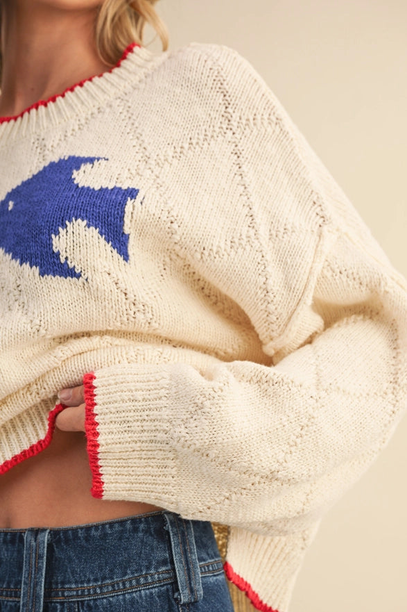 White sweater with blue fish design and red trim worn by a person.