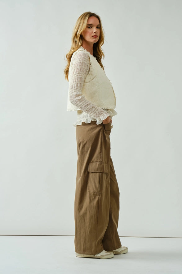 Woman wearing a white lace top and brown wide-leg pants on a plain background