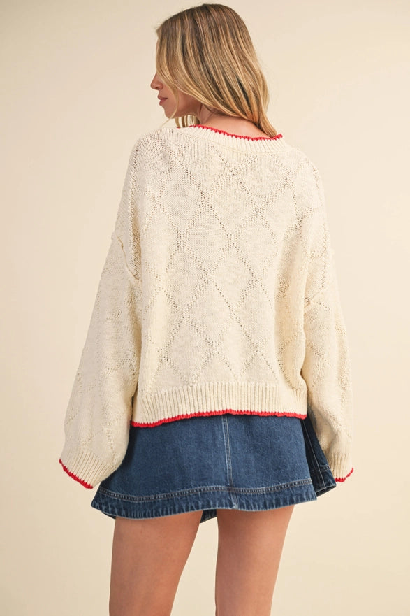 Woman wearing a cream sweater with red trim and a denim skirt on a beige background