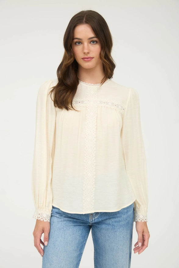 Woman wearing a cream blouse with lace trim and light blue jeans on a white background