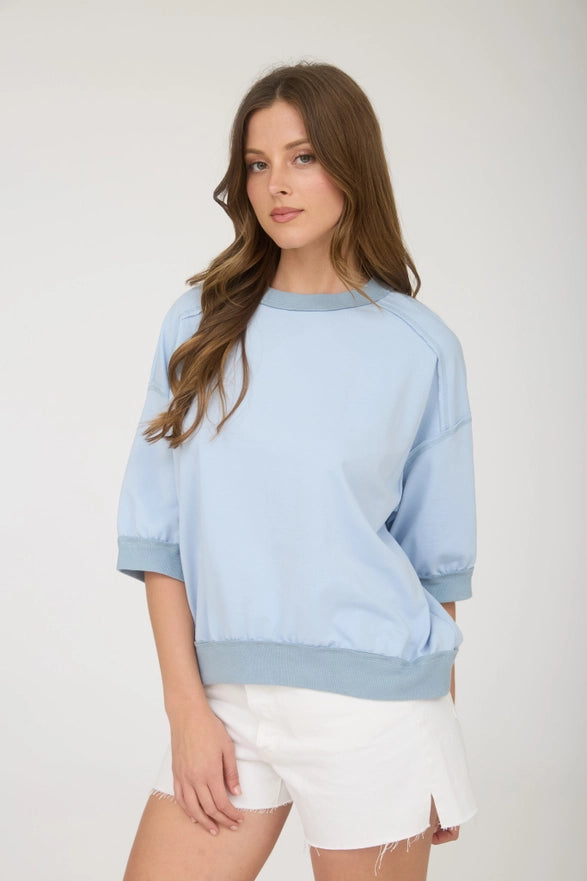 Woman wearing a light blue sweatshirt and white shorts on a plain background