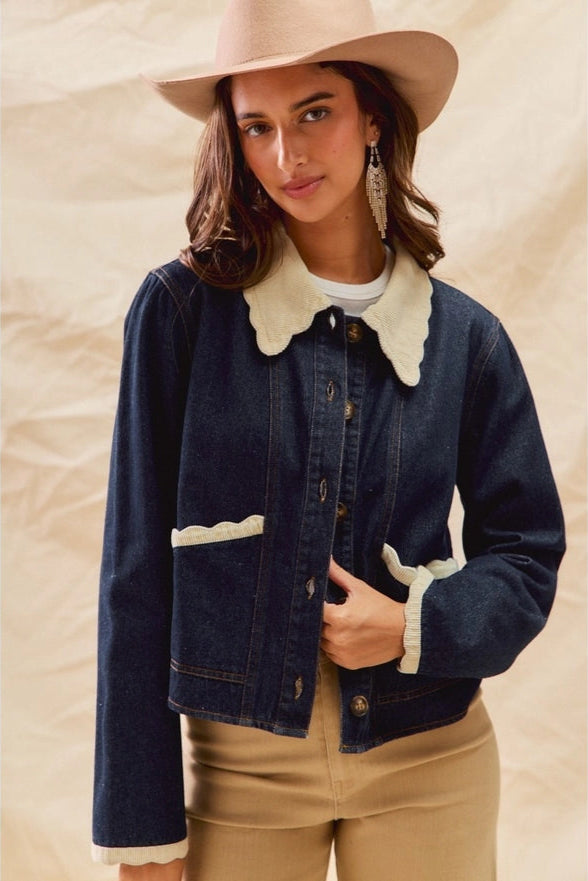 Woman wearing a denim jacket with white trim, beige hat, and pants against a beige background