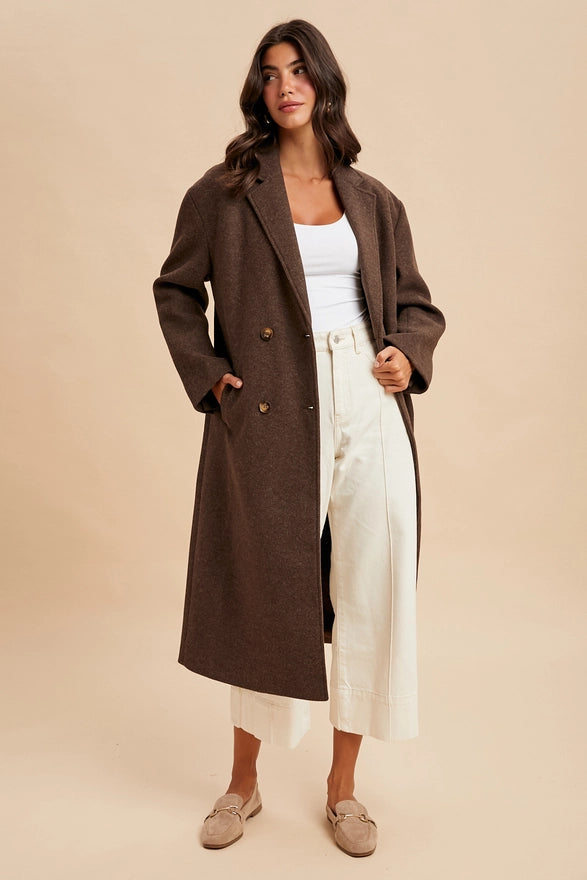 Woman wearing a brown coat over a white top and pants on a beige background