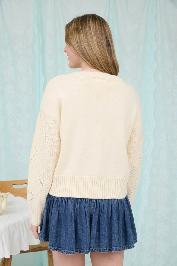 Woman wearing a cream sweater and blue skirt against a light blue curtain background