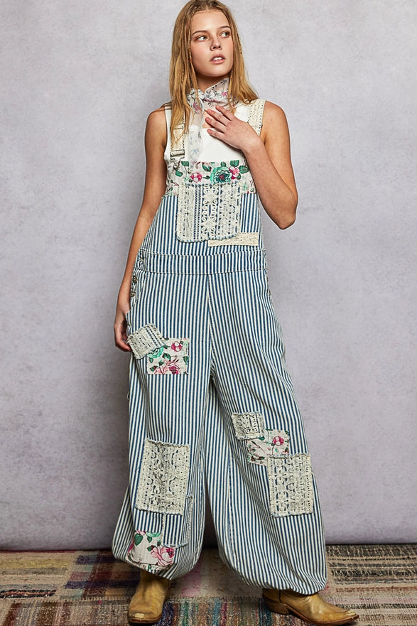 Person wearing a sleeveless floral top and striped overalls with patchwork design against a plain background.