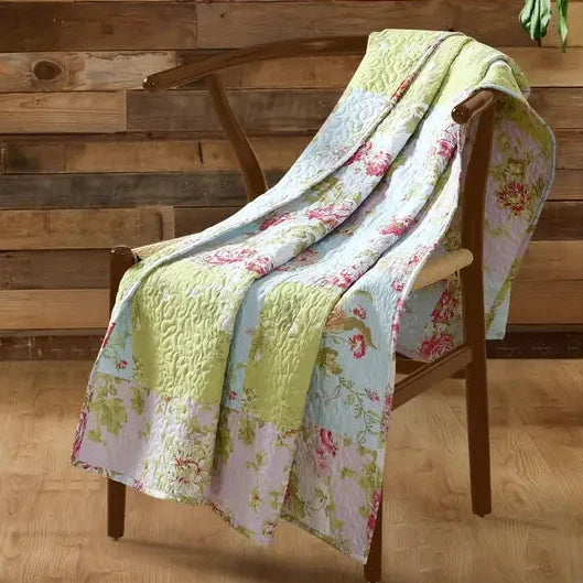 Floral quilt draped over a wooden chair against a wooden wall.