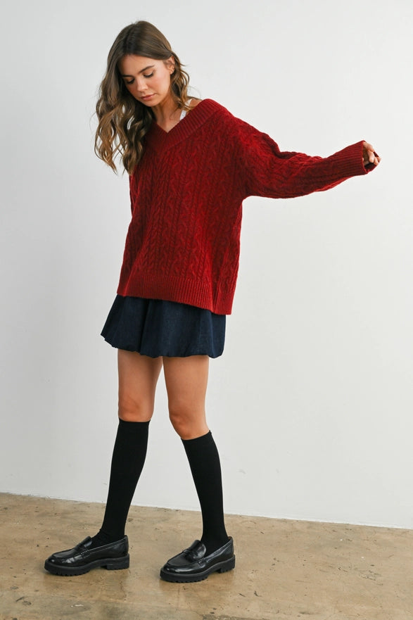 Girl Standing against a plain background wearing a V neck Wine Blue cable knit sweater with long sleeve