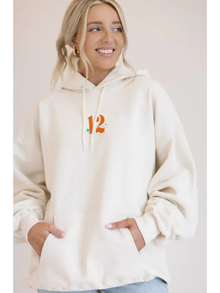 Woman wearing a cream hoodie with an orange logo on a plain background