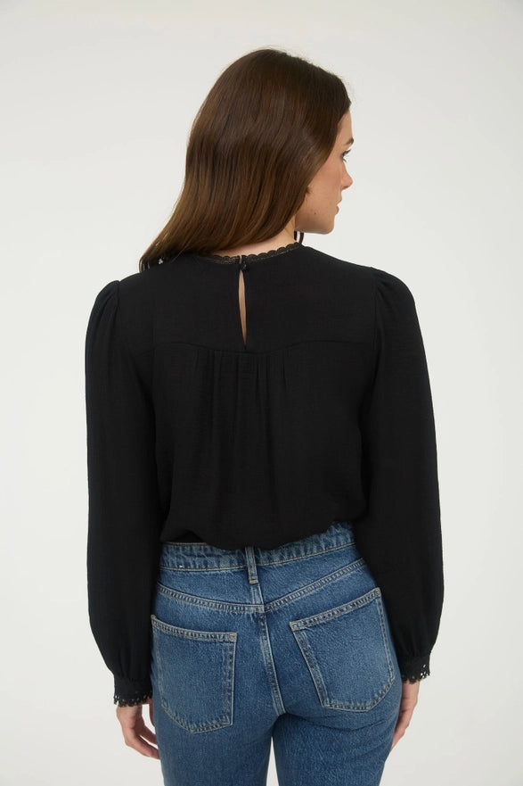 Woman wearing a black blouse with lace details and blue jeans on a white background