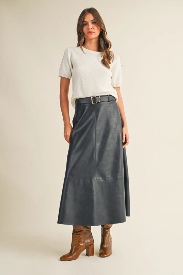 Woman wearing a white top, black leather skirt, and brown boots on a beige background
