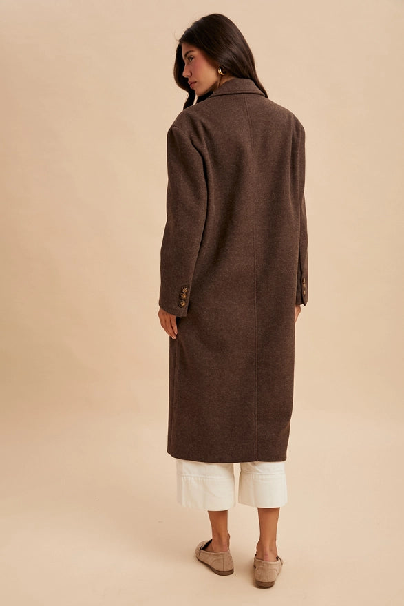 Woman wearing a long brown coat against a beige background