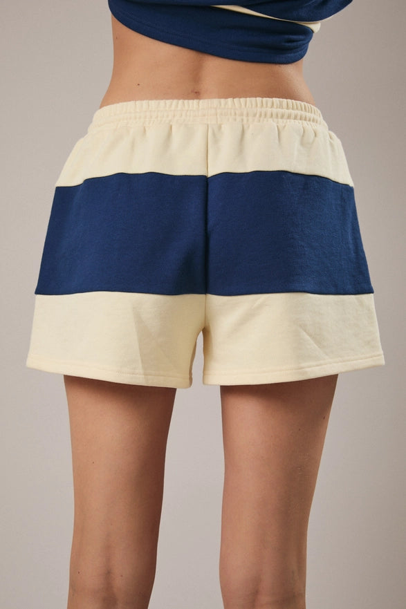Model is wearing a matching cream and navy striped set with shorts and a half zip polo like top.